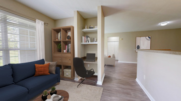 Study Area of an apartment with a round black table with chairs on a carpeted floor overlooking a small kitchen in an open-concept room